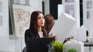 portret van architect aan het studeren 3d gebouw model- voor afmetingen, op zoek Bij gedrukt maquette naar vertalen dimensies in coworking ruimte. Aziatisch ingenieur werken Aan industrieel bouw. video