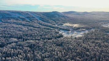 Top view of ski base with slopes on mountain. Footage. Panorama of snow-covered mountains with ski slopes and recreation among coniferous forest on clear winter day video