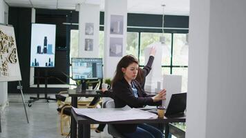 arquitetônico técnico examina 3d construção modelo dentro criativo agência coworking espaço, levando notas do Projeto linhas e Medidas. mulher medindo maquete escala e elementos. tripé tomada. video