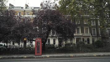 traditionnel rouge Téléphone des boites dans Londres permanent sur le rue près le route contre le des arbres. nationale symboles de Angleterre video