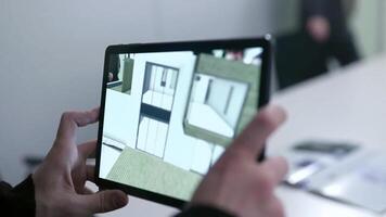 virtuel dessin de maison sur tablette. action. homme d'affaire en portant tablette avec virtuel réalité projet à Accueil dans salle de réunion. numérique 3d modèle de réel biens projet est montré sur gadget video