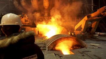 Rückseite Aussicht von ein Arbeiter im feuerfest Uniform und ein Ingenieur Stehen im Vorderseite von Arbeiten sprengen Ofen beim das Fabrik. Lager Filmaufnahme. Aussicht Innerhalb von metallurgisch Herstellung Geschäft. video