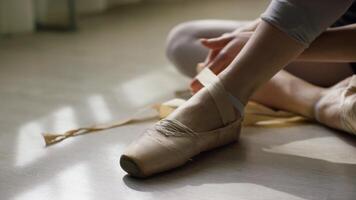 avvicinamento di di ballerina piedi. ballerina preparazione per addestramento, e legatura nastro di pointe scarpe seduta su pavimento nel luminosa luce del sole video