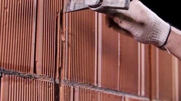 dichtbij omhoog van een Mens hameren de muur gemaakt van keramisch blokken Bij de bouw plaats. voorraad filmmateriaal. arbeider in beschermend handschoenen maken een gat in de muur. video