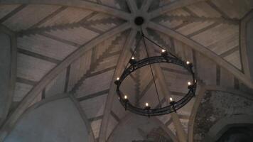 View from the bottom on the old chandelier in the form of a wheel with light bulbs hanging on the ceiling in church or another old building. Action. Beautiful retro style video