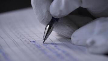 lado ver de un mano haciendo notas en un cuaderno. valores imágenes. cerca arriba de manos en blanco guantes escritura datos en el cuaderno con un bolígrafo en negro antecedentes. video