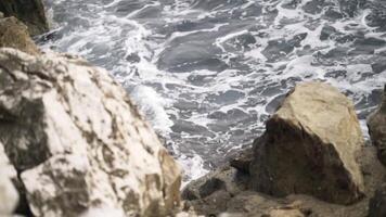 Close-up of grey waves with foam breaking on the rocks in the sea. Action. View to the sea from rock. video