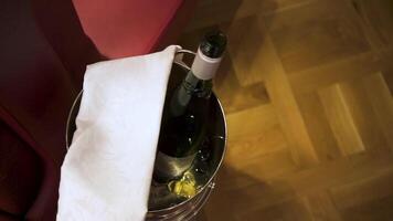 Close up of opened champagne bottle in ice bucket with white towel on brown floor background, room service concept. Stock footage. Bottle of wine in the bucket, top view. video