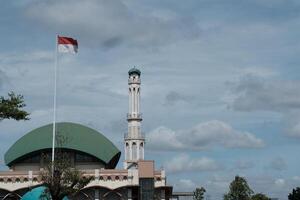 a mosque with indonesian flag in front of it on the cloudy weather photo