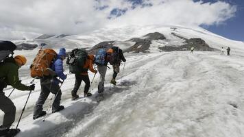 Climbers climb snowy mountain. Clip. Climbers follow each other in line to snowy peak on clear day. Group of climbers ascend snowy mountain on background of blue sky photo