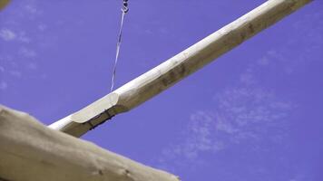 Crane lifts beam on background of blue sky. Clip. Crane at construction site lifts heavy treated wood to construction site photo