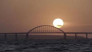 Stunning view of the beautiful sunset over the big river and the bridge, time lapse effect. Shot. Bright golden sun moving towards the horizon above the river. photo