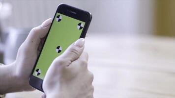 Young woman with beautiful manicure holding iPhone in hands and typing on the chroma key green screen. Stock footage. Technology, mockup and internet concept photo