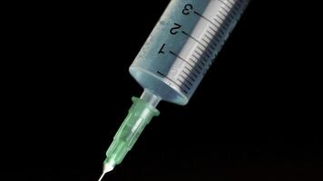 Taking vaccine into a glass syringe from a ampule on a black background. Closeup. Syringe is typed in turquoise fluid injection from illness serious illnesses, the concept of medicine photo