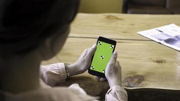 cerca arriba de niña sentado a el mesa y utilizando teléfono inteligente con verde pantalla. valores imágenes. ver terminado el hombro de un mujer en el dispositivo con clave de croma foto