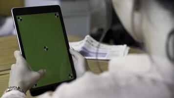 Rear view of a woman holding a tablet with chromakey with tracking marks on wooden table background. Stock footage. Different action with the device in daylight indoor space, green screen. photo