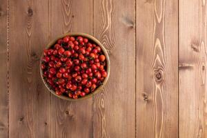 red dog-rose rosehip fruits in a wooden bowl on wooden table photo