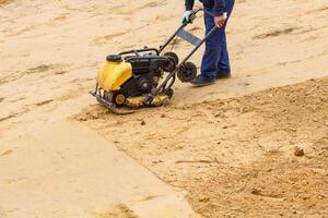 Worker using vibratory plate compactor for compaction sand during path construction. photo