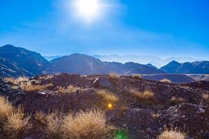 rocks and dry grass tufts in autumn mountains backlit scene at sunny day photo