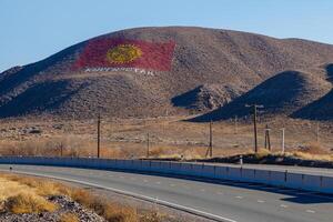 The flag of Kyrgyzstan is drawn on a mountain at sunny autumn day, showcasing the nation's pride and spirit. photo