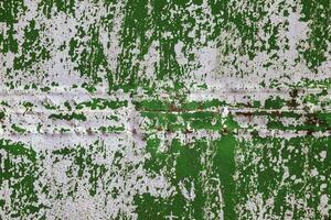 green steel sheet wall with peeled off white paint under direct sunlight, full-frame background and texture photo