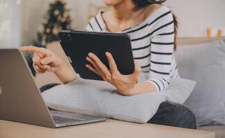 joven atractivo asiático mujer descansando utilizando hojeada tableta computadora en sofá a hogar, contento niña sentado en sofá relajarse leyendo digital artilugio con entusiasmado, comunicación y estilo de vida concepto. foto