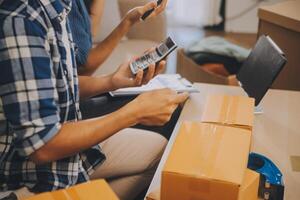 Two Asian blogger showing clothes in front of the camera to recording vlog video live streaming at her shop. Online Shopping Cart notion. on sofa at home photo