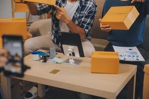 Two Asian blogger showing clothes in front of the camera to recording vlog video live streaming at her shop. Online Shopping Cart notion. on sofa at home photo
