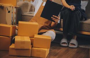 Two Asian blogger showing clothes in front of the camera to recording vlog video live streaming at her shop. Online Shopping Cart notion. on sofa at home photo