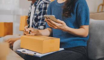 Two Asian blogger showing clothes in front of the camera to recording vlog video live streaming at her shop. Online Shopping Cart notion. on sofa at home photo
