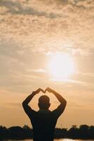 Hand heart frame shape silhouette made against the sun sky of a sunrise or sunset on photo