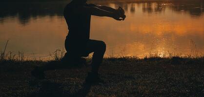 Back view silhouette of a runner man running on the beach at sunset with sun in the background photo