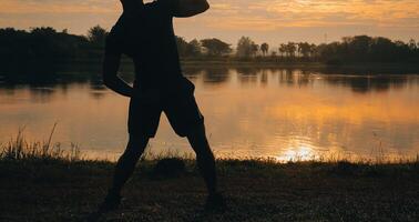 Back view silhouette of a runner man running on the beach at sunset with sun in the background photo