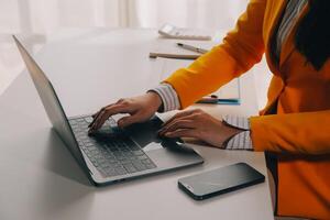 negocio mujer utilizando móvil teléfono durante trabajando en ordenador portátil computadora, surf el Internet, buscando negocio datos a moderno oficina. asiático mujer de negocios en línea trabajando en computadora a lugar de trabajo foto