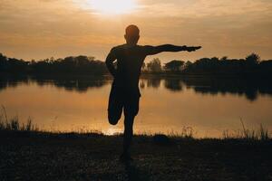 Back view silhouette of a runner man running on the beach at sunset with sun in the background photo