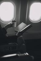 rubia hembra turista comprobación entrante notificación en teléfono inteligente sentado en asiento de avión con netbook.joven mujer de negocios compartir medios de comunicación desde teléfono en ordenador portátil computadora durante avión vuelo foto