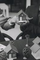 agente de corretaje de bienes raíces entrega una muestra de una casa modelo al cliente, contrato de préstamo hipotecario que arrienda y compra y vende casa y contrata el concepto de préstamo hipotecario de seguro de hogar foto