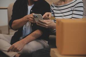 Two Asian blogger showing clothes in front of the camera to recording vlog video live streaming at her shop. Online Shopping Cart notion. on sofa at home photo