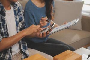 Two Asian blogger showing clothes in front of the camera to recording vlog video live streaming at her shop. Online Shopping Cart notion. on sofa at home photo