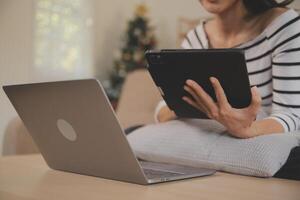 joven atractivo asiático mujer descansando utilizando hojeada tableta computadora en sofá a hogar, contento niña sentado en sofá relajarse leyendo digital artilugio con entusiasmado, comunicación y estilo de vida concepto. foto