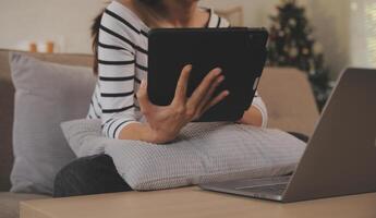 joven atractivo asiático mujer descansando utilizando hojeada tableta computadora en sofá a hogar, contento niña sentado en sofá relajarse leyendo digital artilugio con entusiasmado, comunicación y estilo de vida concepto. foto