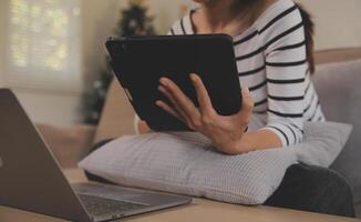 joven atractivo asiático mujer descansando utilizando hojeada tableta computadora en sofá a hogar, contento niña sentado en sofá relajarse leyendo digital artilugio con entusiasmado, comunicación y estilo de vida concepto. foto