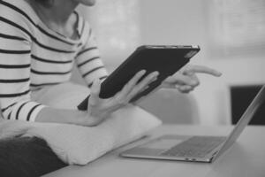 joven atractivo asiático mujer descansando utilizando hojeada tableta computadora en sofá a hogar, contento niña sentado en sofá relajarse leyendo digital artilugio con entusiasmado, comunicación y estilo de vida concepto. foto