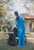 Young asian care helper with asia elderly woman on wheelchair relax together park outdoors to help and encourage and rest your mind with green nature. Help support yourself to learn to walk. walker photo