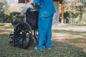 Young asian care helper with asia elderly woman on wheelchair relax together park outdoors to help and encourage and rest your mind with green nature. Help support yourself to learn to walk. walker photo