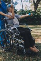 Young nurse or physiotherapist in scrubs helping a happy retired old woman do fitness exercises with light weight dumbbells at home. Concept of physiotherapy for seniors photo