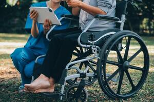 Elderly asian senior woman on wheelchair with Asian careful caregiver and encourage patient, walking in garden. with care from a caregiver and senior health insurance in sun light photo