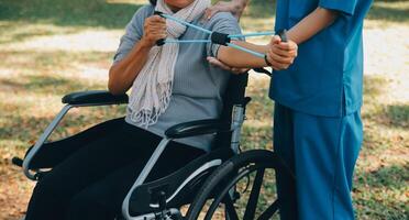 Young nurse or physiotherapist in scrubs helping a happy retired old woman do fitness exercises with light weight dumbbells at home. Concept of physiotherapy for seniors photo