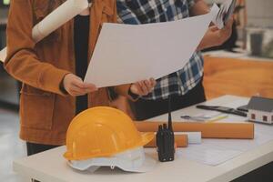 masculino y hembra industrial ingenieros en difícil sombreros discutir nuevo proyecto mientras utilizando ordenador portátil. ellos hacer demostración gestos ellos trabajo en un pesado industria fabricación fábrica. foto