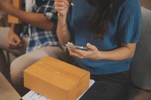 Two Asian blogger showing clothes in front of the camera to recording vlog video live streaming at her shop. Online Shopping Cart notion. on sofa at home photo